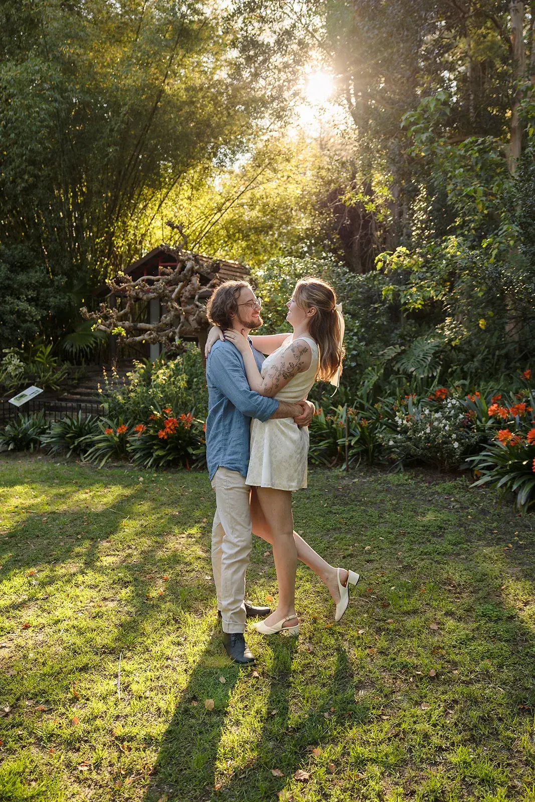 Arden and Kobi embracing on the lawn as the sun sets through the trees at Wanneroo Botanic Gardens