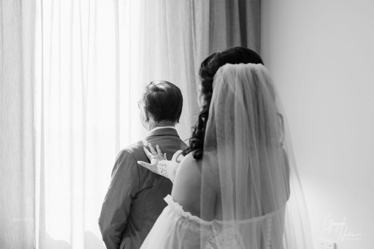 Bride in a veil gently touches a man’s shoulder in front of a bright curtain, creating an emotional moment. Black and white photo.