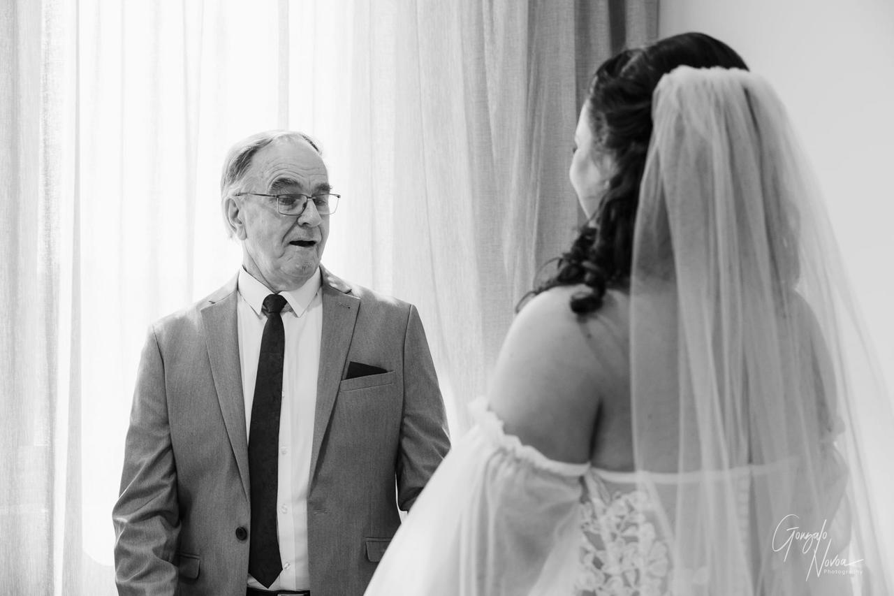 Older man in suit looks surprised at a woman in a wedding dress. Bright background with curtains. Emotional and heartwarming scene.