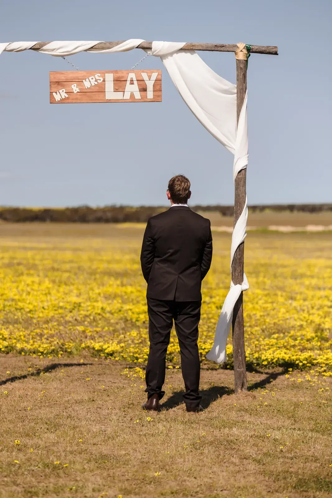 Jason waits at the arbour with his back to the aisle