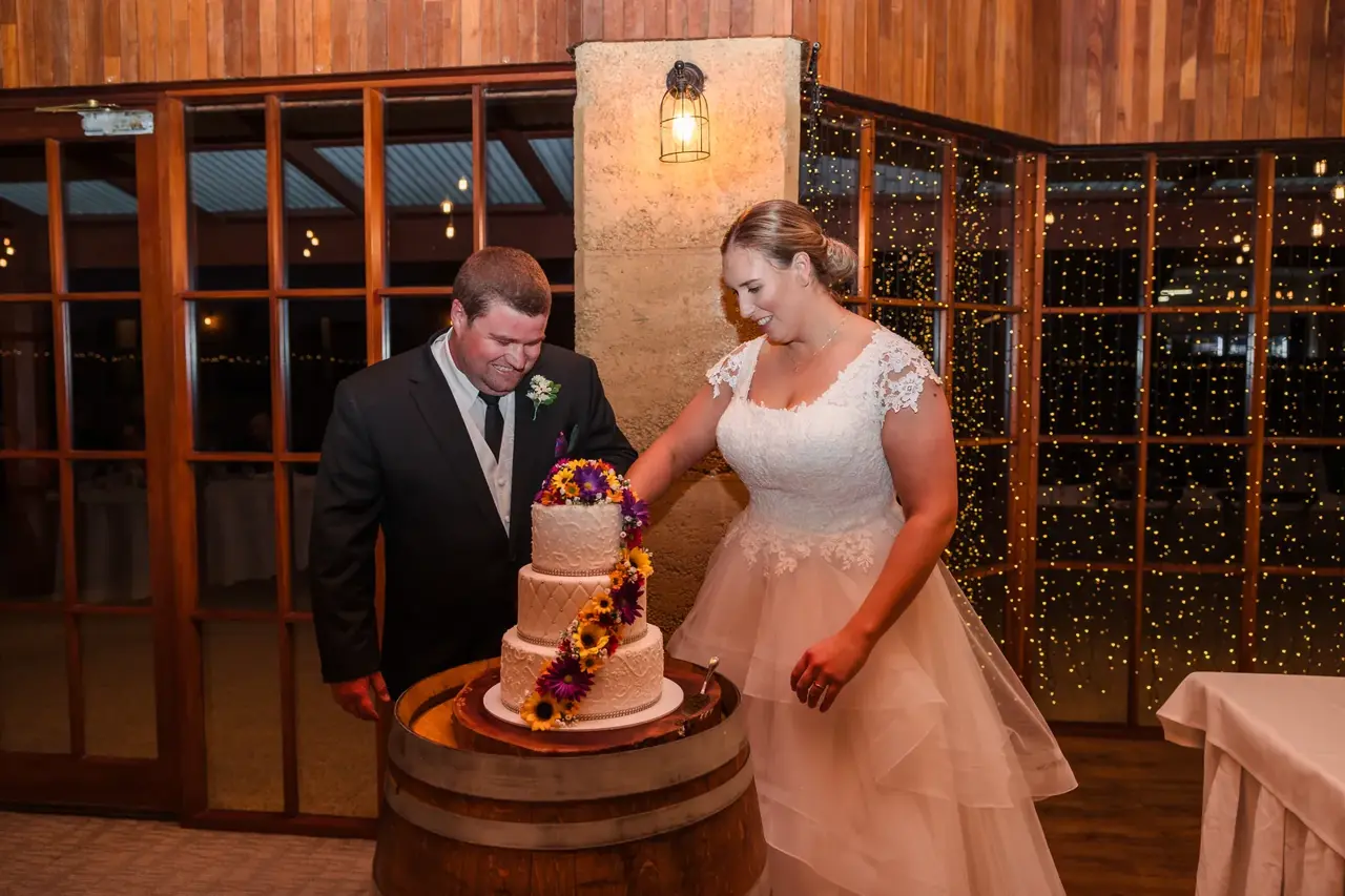 Sarah and James cut their flower-trimmed wedding cake on a wine barrel in the Homestead at Quarry Farm