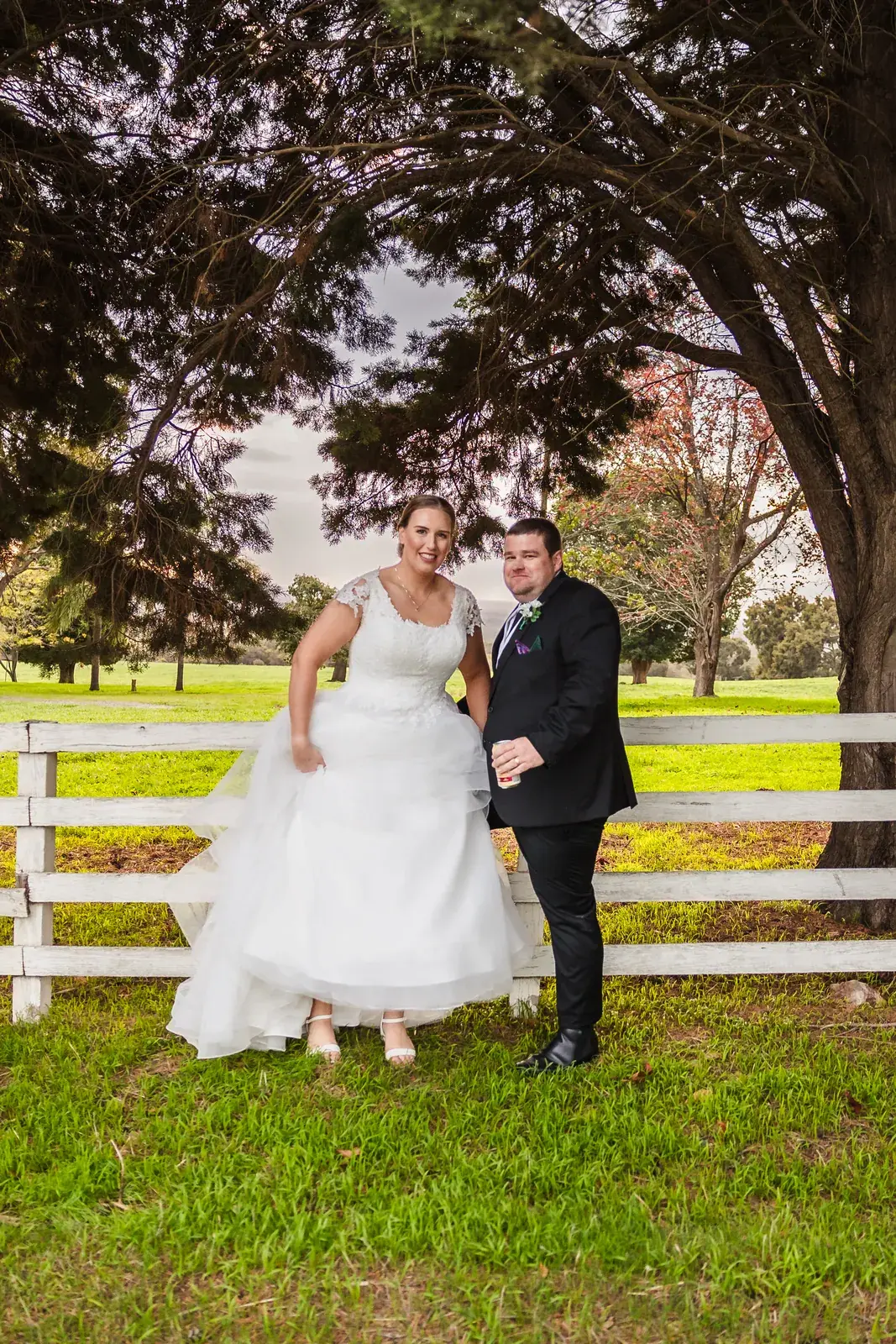 Sarah and James recreate her parents' wedding photo at the white timber fence at Quarry Farm
