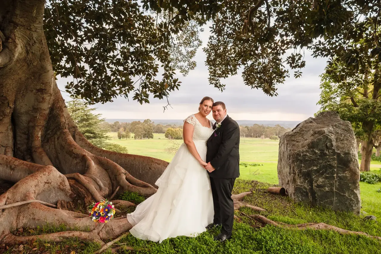 Sarah and James stand in the roots of the huge wild fig tree beside a standing stone at Quarry Farm