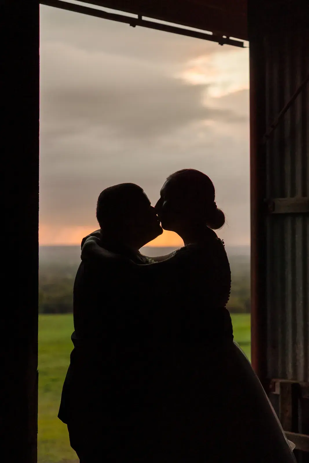 Sarah and James kiss in silhouette in the shearing shed doorway at Quarry Farm