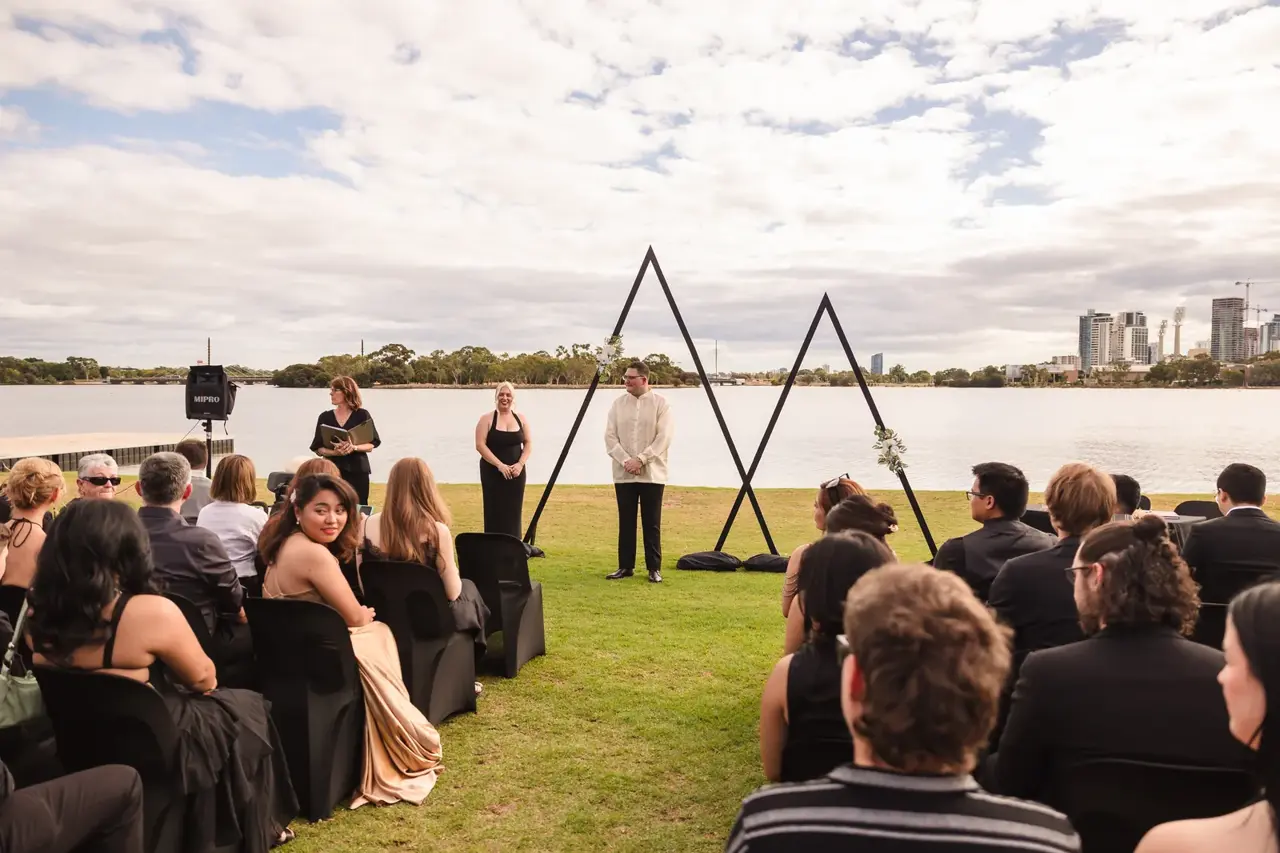 Guests seated on the riverside lawn for a ceremony with the Swan River and Perth skyline behind at Burswood on Swan