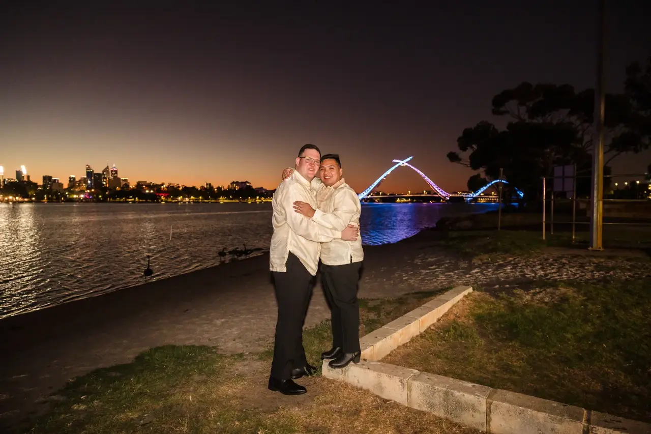 A couple by the Swan River at night with the lit Matagarup bridge behind at Burswood on Swan
