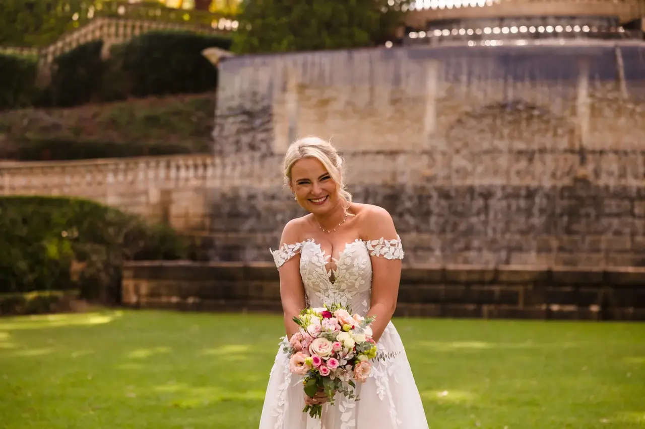 Rosie holds her bouquet in front of a stone wall and hedges at Caversham House