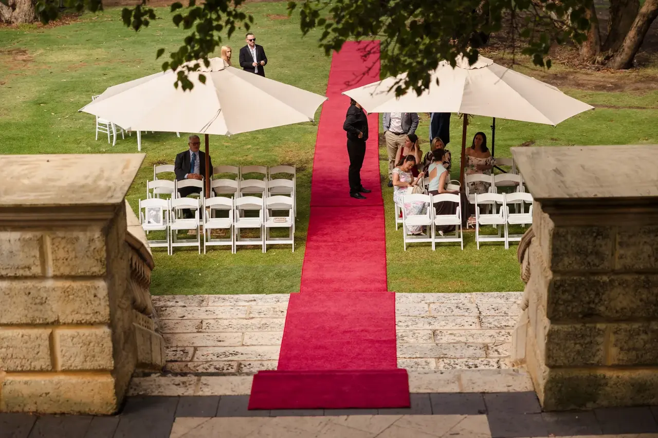 A red carpet and white chairs under sunshades on the ceremony lawn at Caversham House