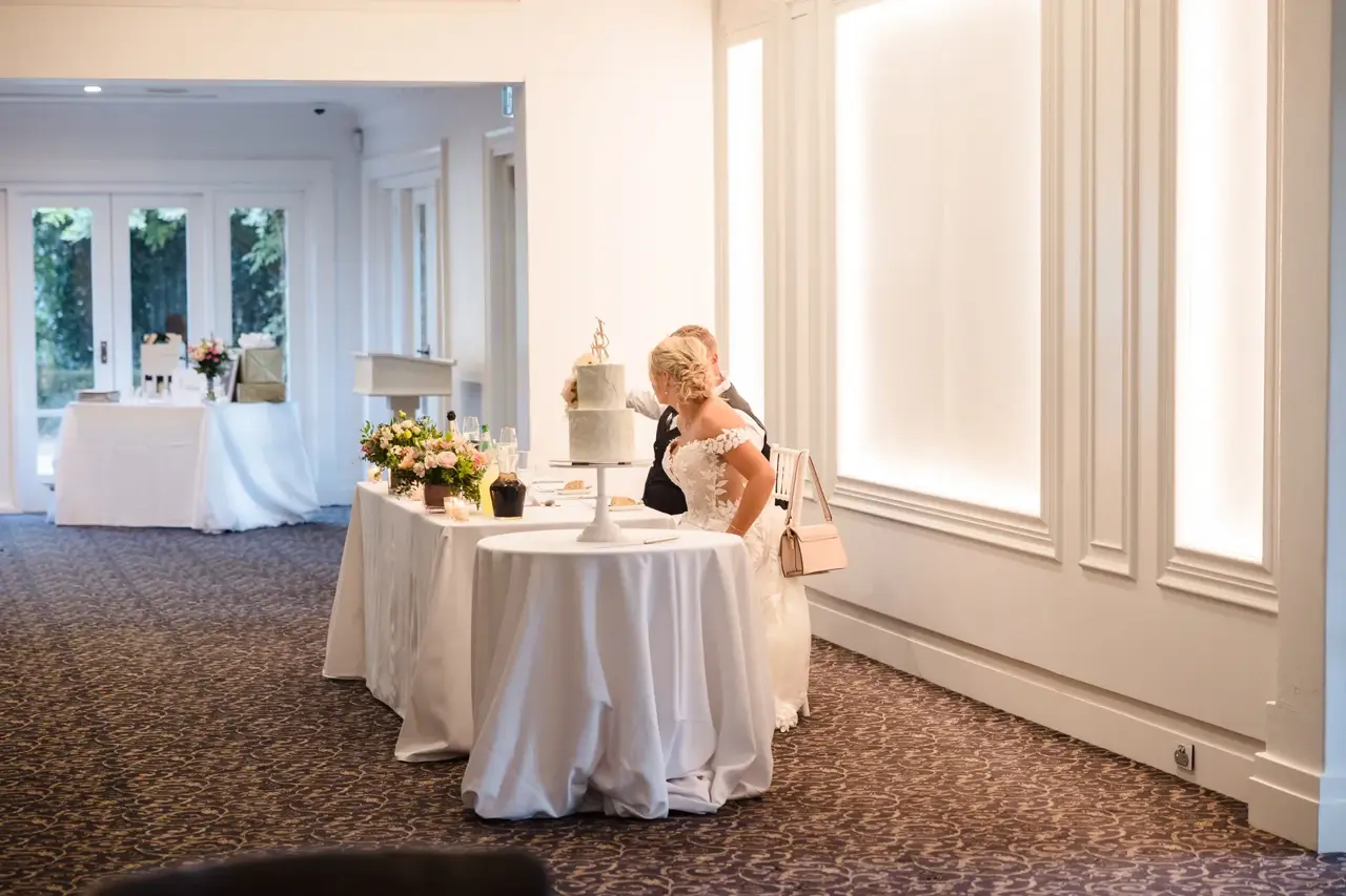 Rosie and Adam at their table beside the wedding cake in a white reception room at Caversham House