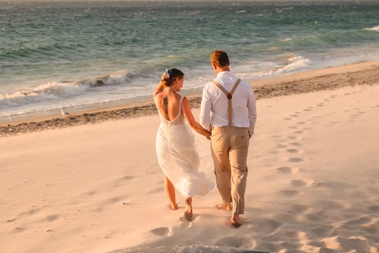 Bride and groom walking toward the ocean on Port Beach at sunset, COAST wedding