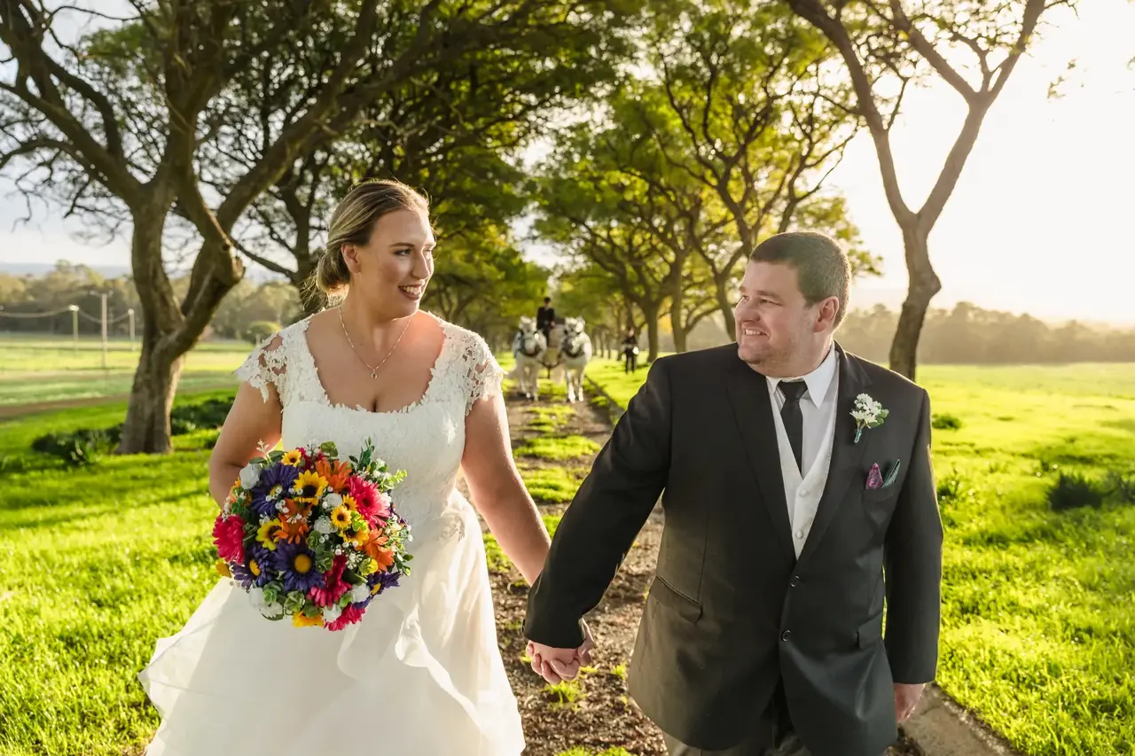 A couple walk hand in hand down the Jacaranda-lined Quarry Lane at golden hour at Quarry Farm