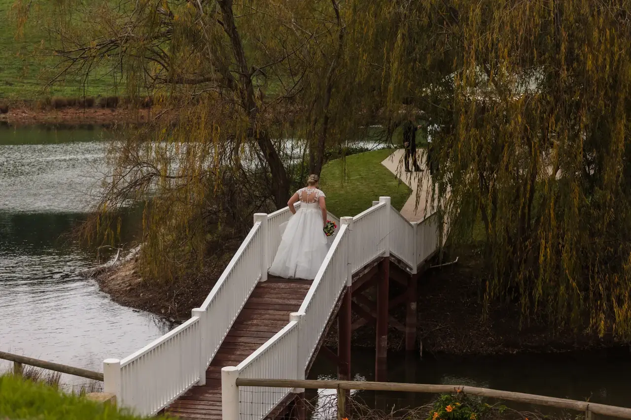 A bride crosses the white timber bridge over the dam at Quarry Farm