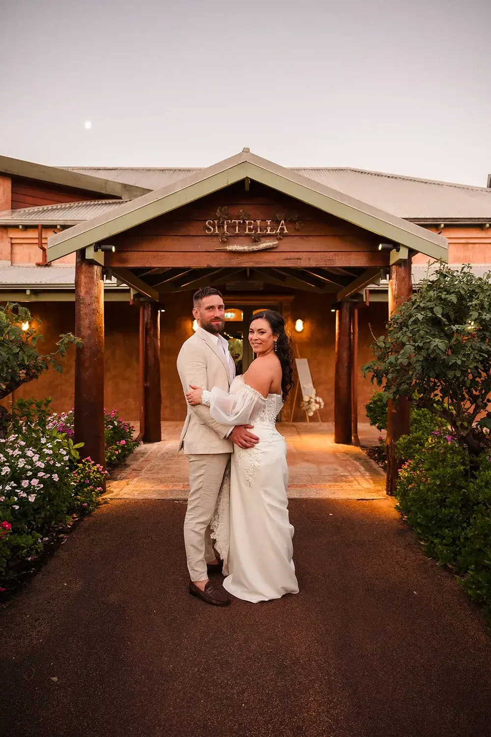 Bride and groom under the lit Sittella Winery timber entrance at dusk