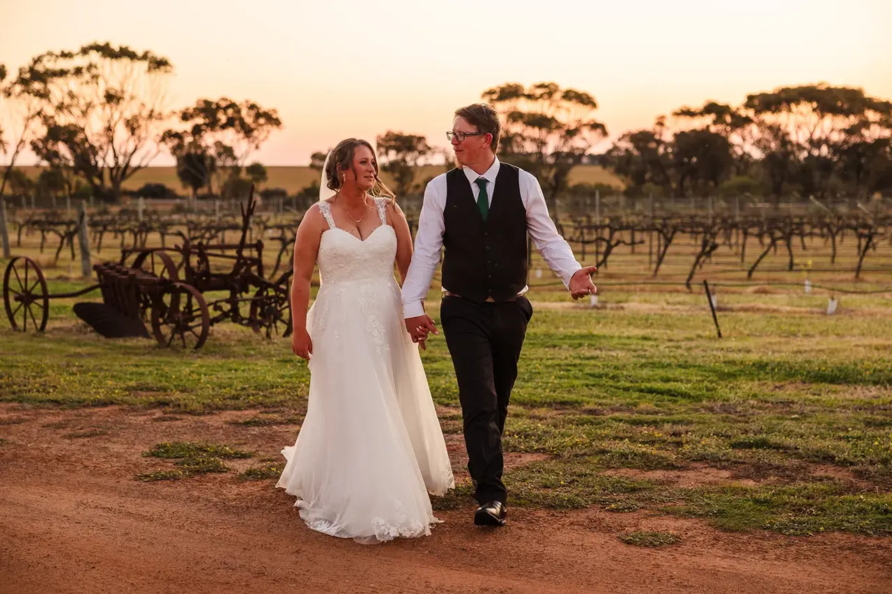 A couple walk past old farm machinery in the vines at sunset at Walkers Hill Vineyard