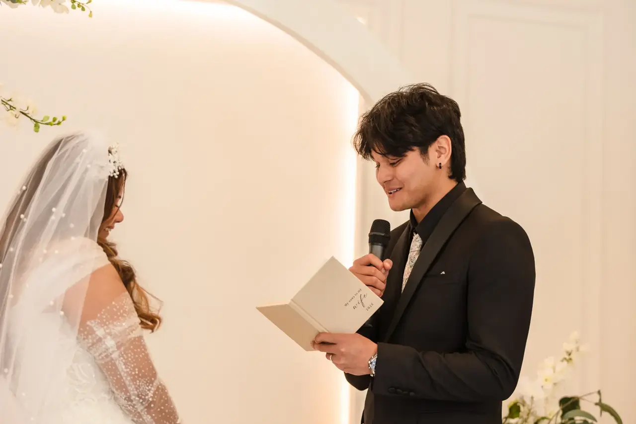 Kusal reads his vows from a card into a microphone as Naila looks on