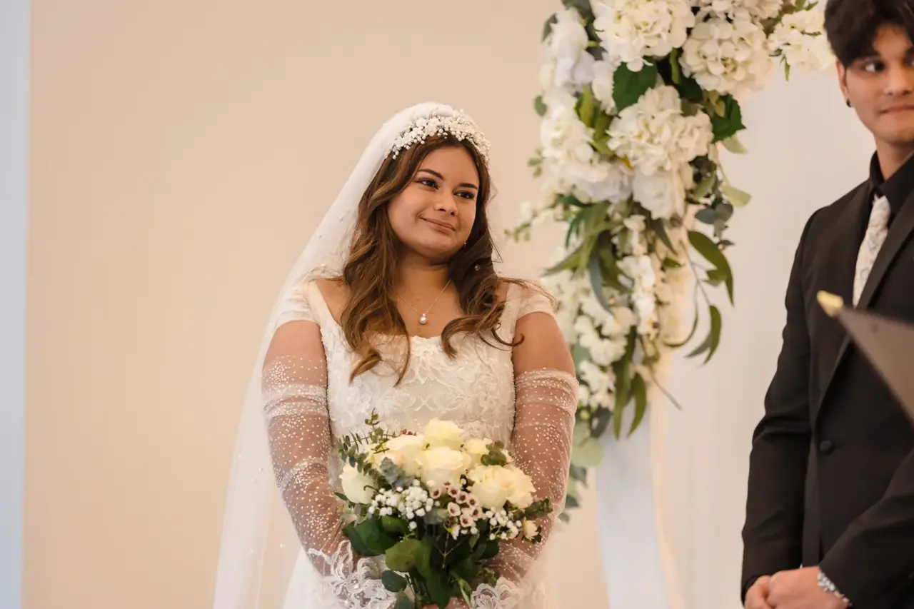 Naila speaks into a microphone during the ceremony, white flowers beside her