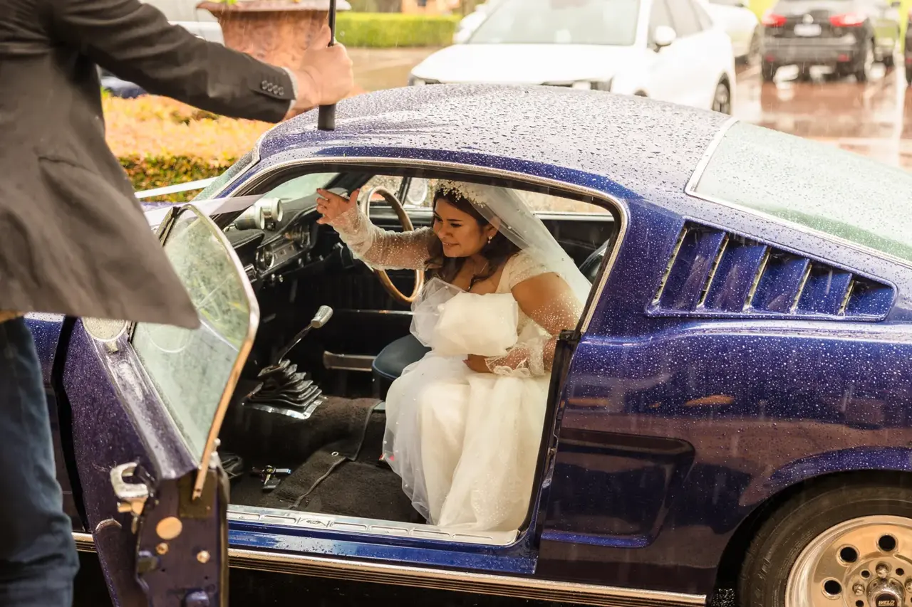 Naila in her veil steps out of the Mustang while an umbrella is held over the door