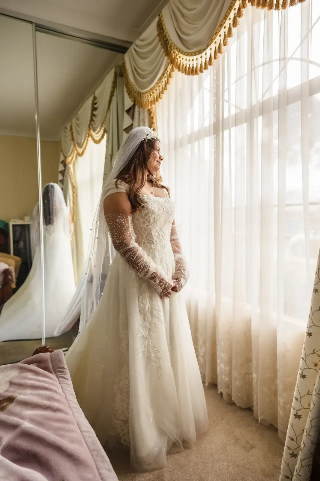 Naila in her dress and veil looks out of a tall window