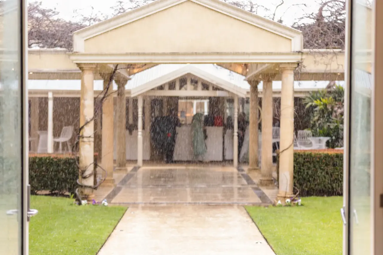 Rain falls past the columned entrance to the Garden House as guests shelter inside