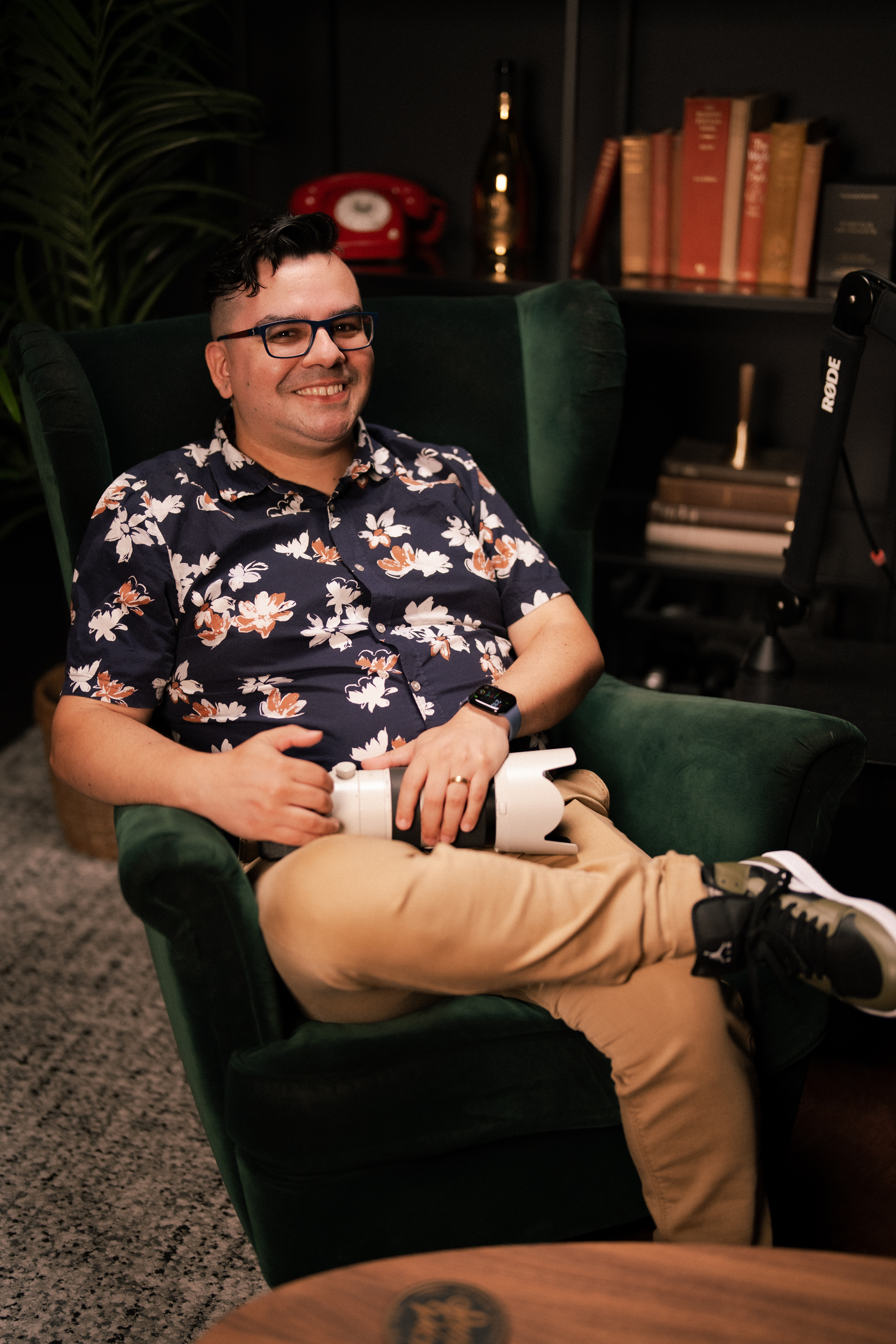 Gonzalo Novoa, Perth wedding photographer, smiling and relaxed in a green armchair holding a camera, wearing a floral shirt