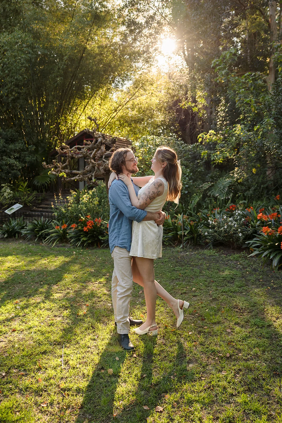 Arden and Kobi embracing on the lawn as the sun sets through the trees at Wanneroo Botanic Gardens
