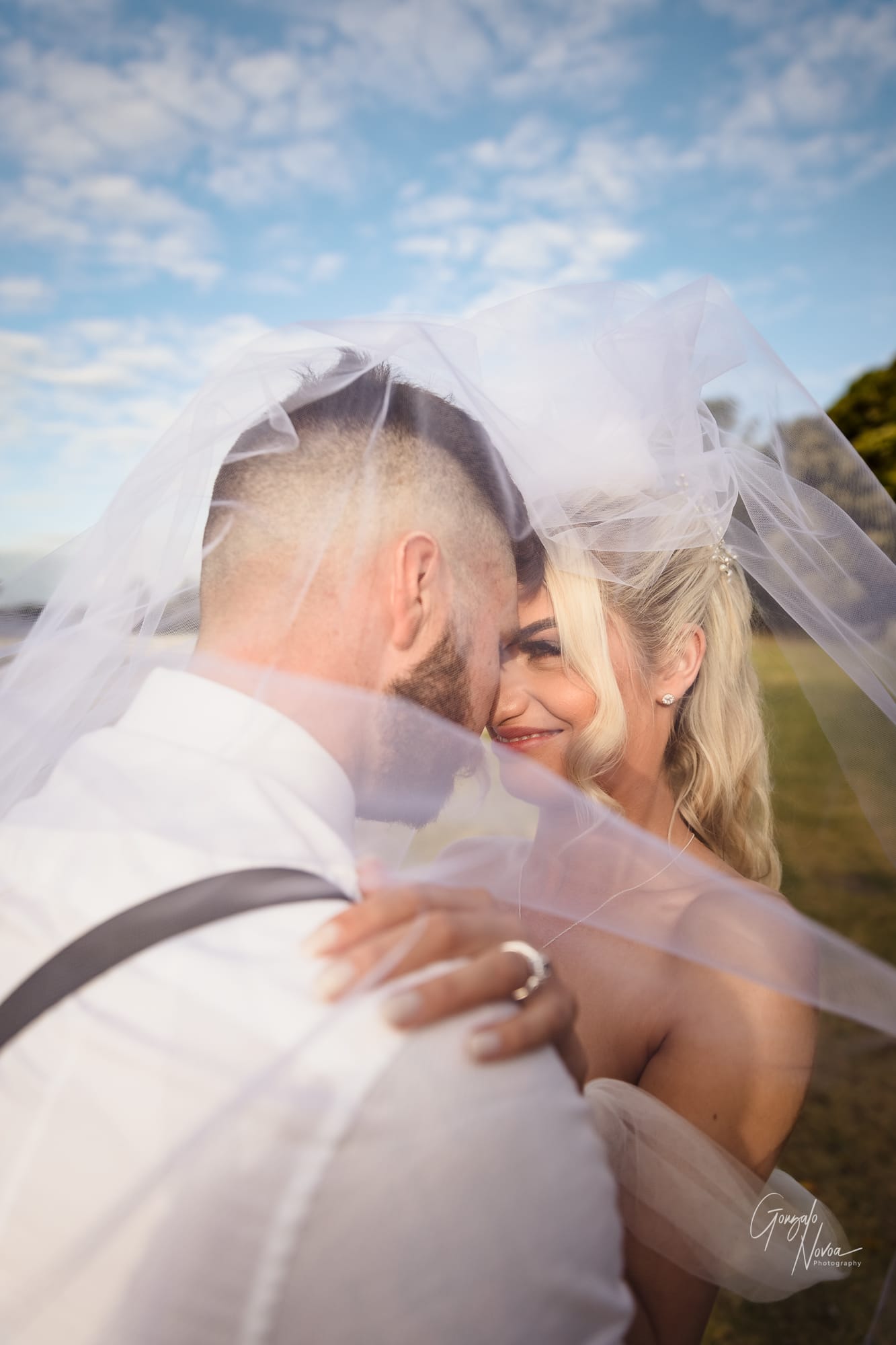 Bride and groom in a close embrace under a flowing white veil in golden hour light
