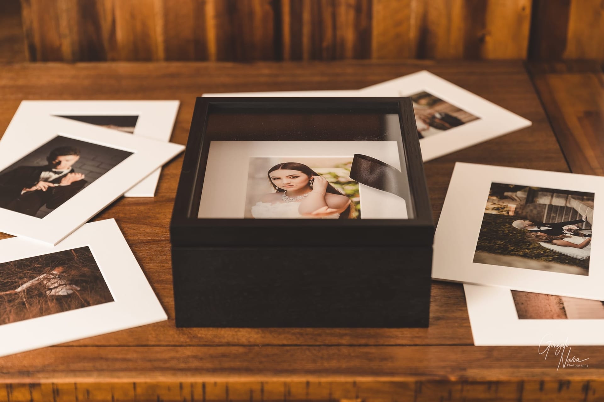 Hand-mande wooden box with clear acrylic lid housing matted prints with additional prints around it over a coffee table
