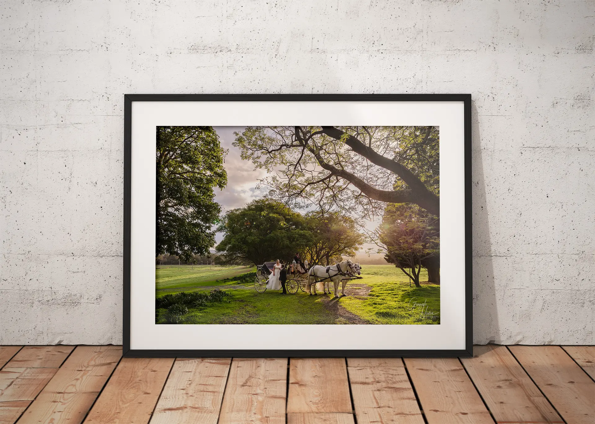 Framed wedding photo of Sarah and James arriving in a white horse-drawn carriage at Quarry Farm, displayed on a timber floor against a textured white wall.