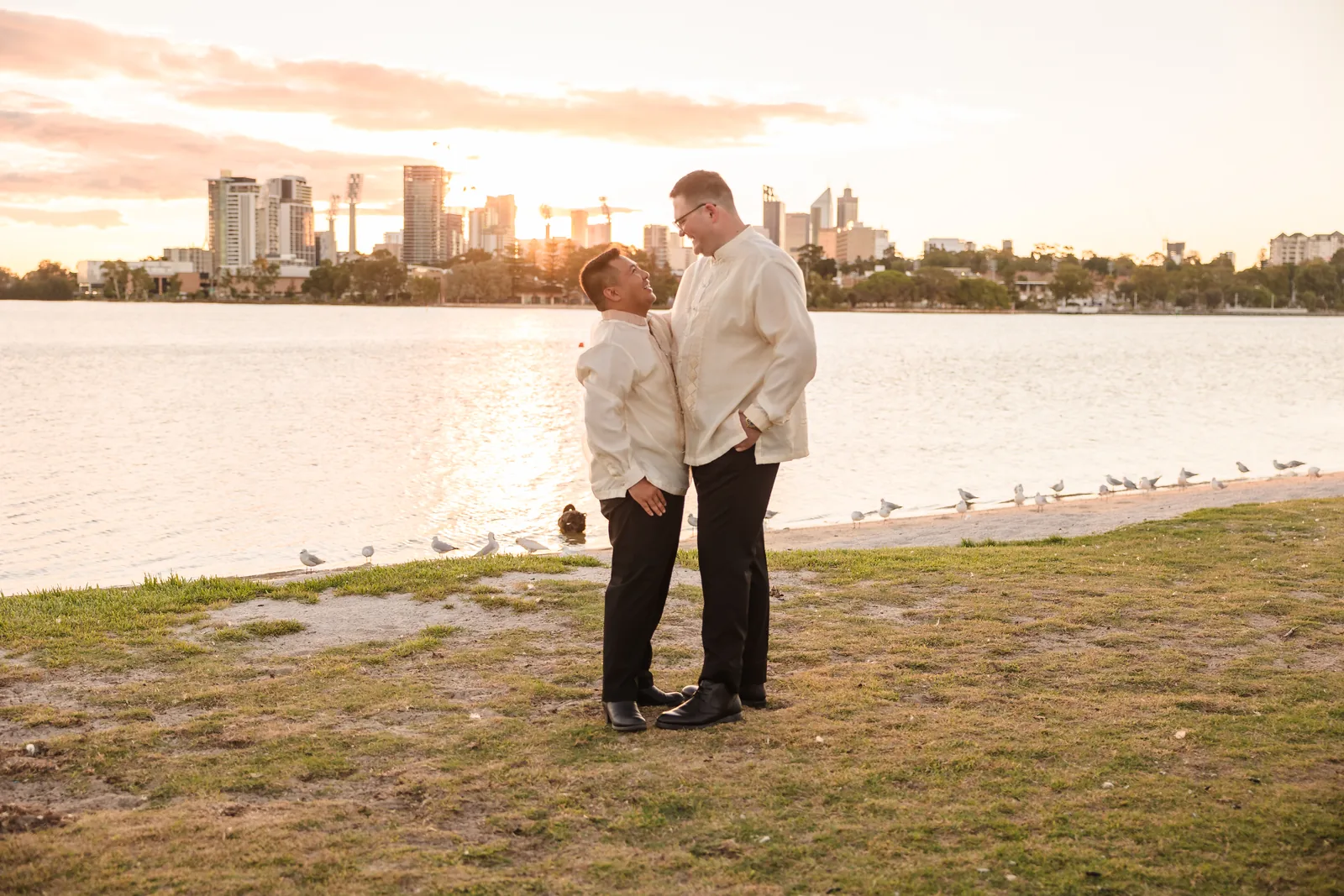 Lloyd and Mitch embracing by the Swan River as the sun sets at Burswood on Swan