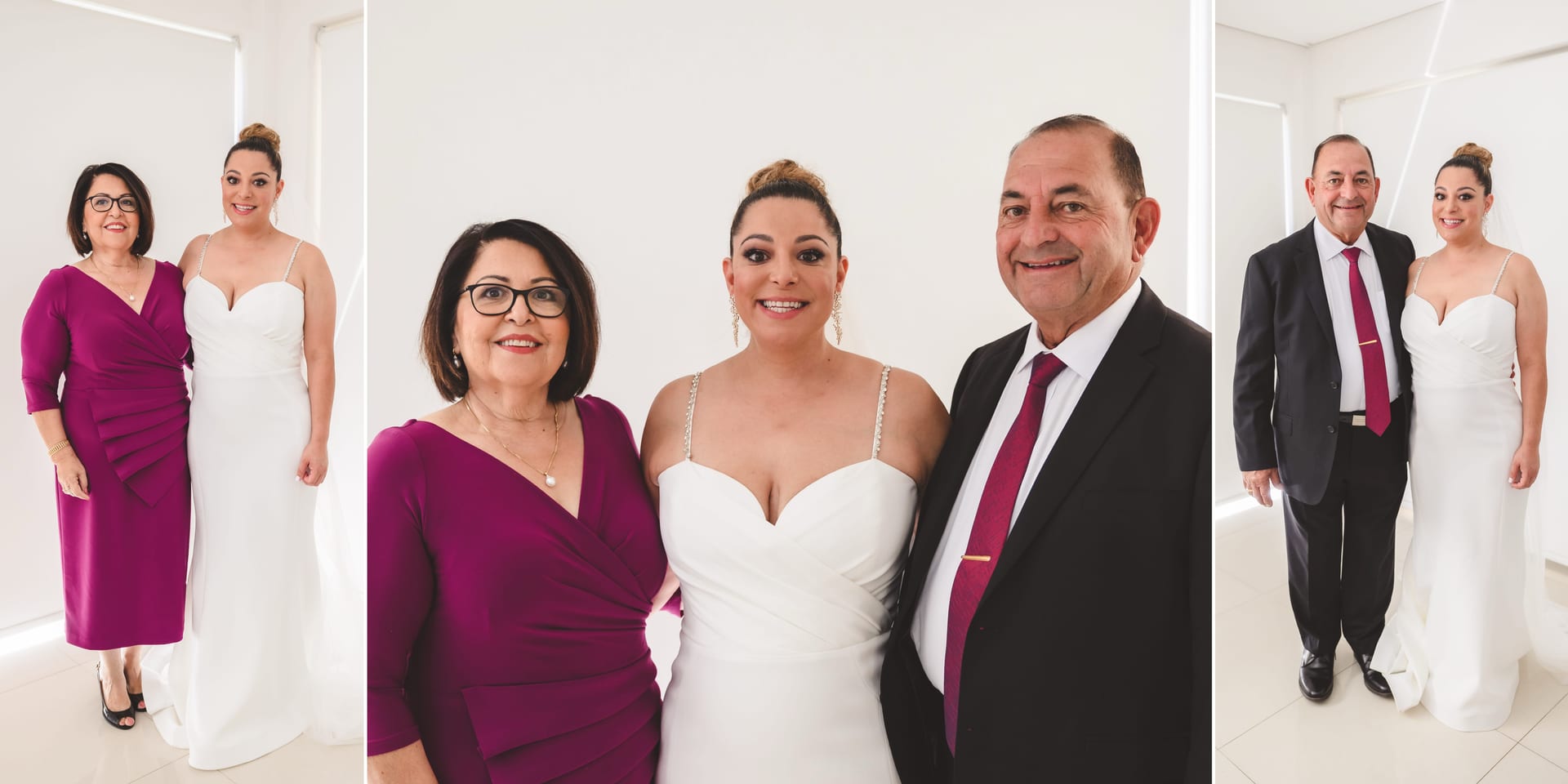 Woman in a white wedding dress with her parents. Mother in a magenta dress, father in a suit and magenta tie. Bright, white background. Smiling.