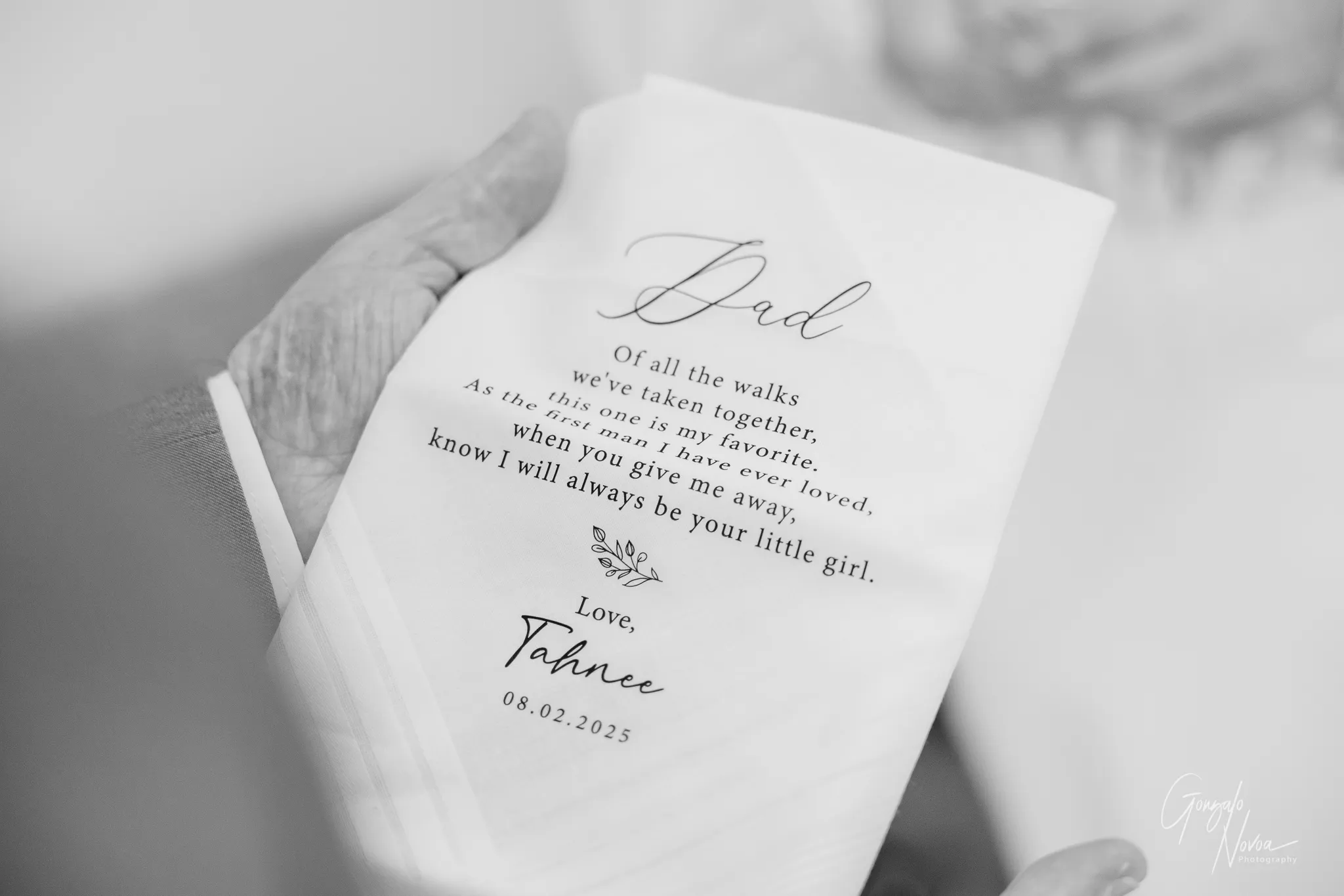 Close-up of a hand holding a personalised wedding handkerchief from bride Tahnee to her father, with a heartfelt message about their bond and her wedding date, 08.02.2025.