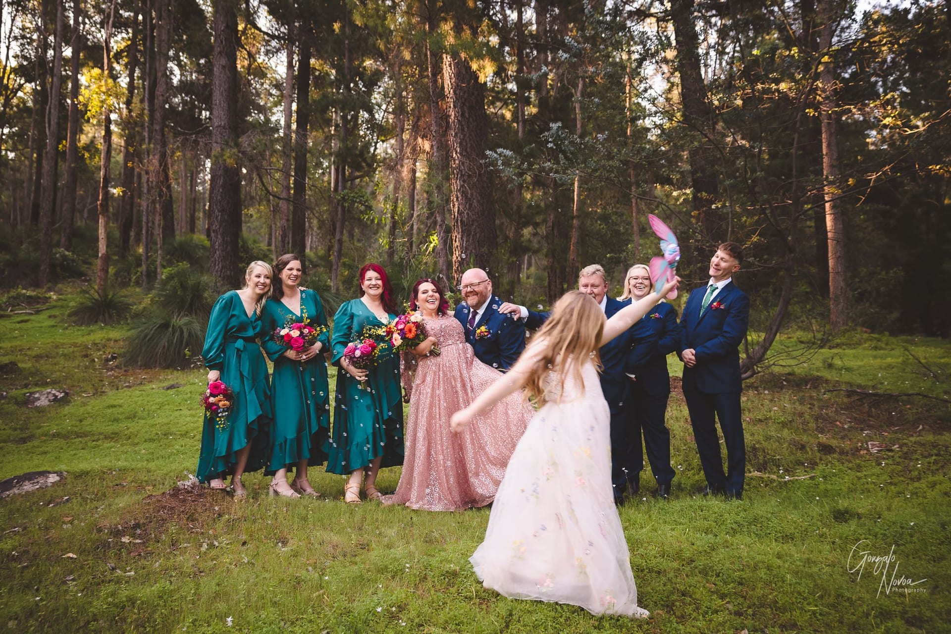 The bridal party in a serene woodland setting, featuring the flower girl walking in front of them shooting bubbles from a bubble gun machine