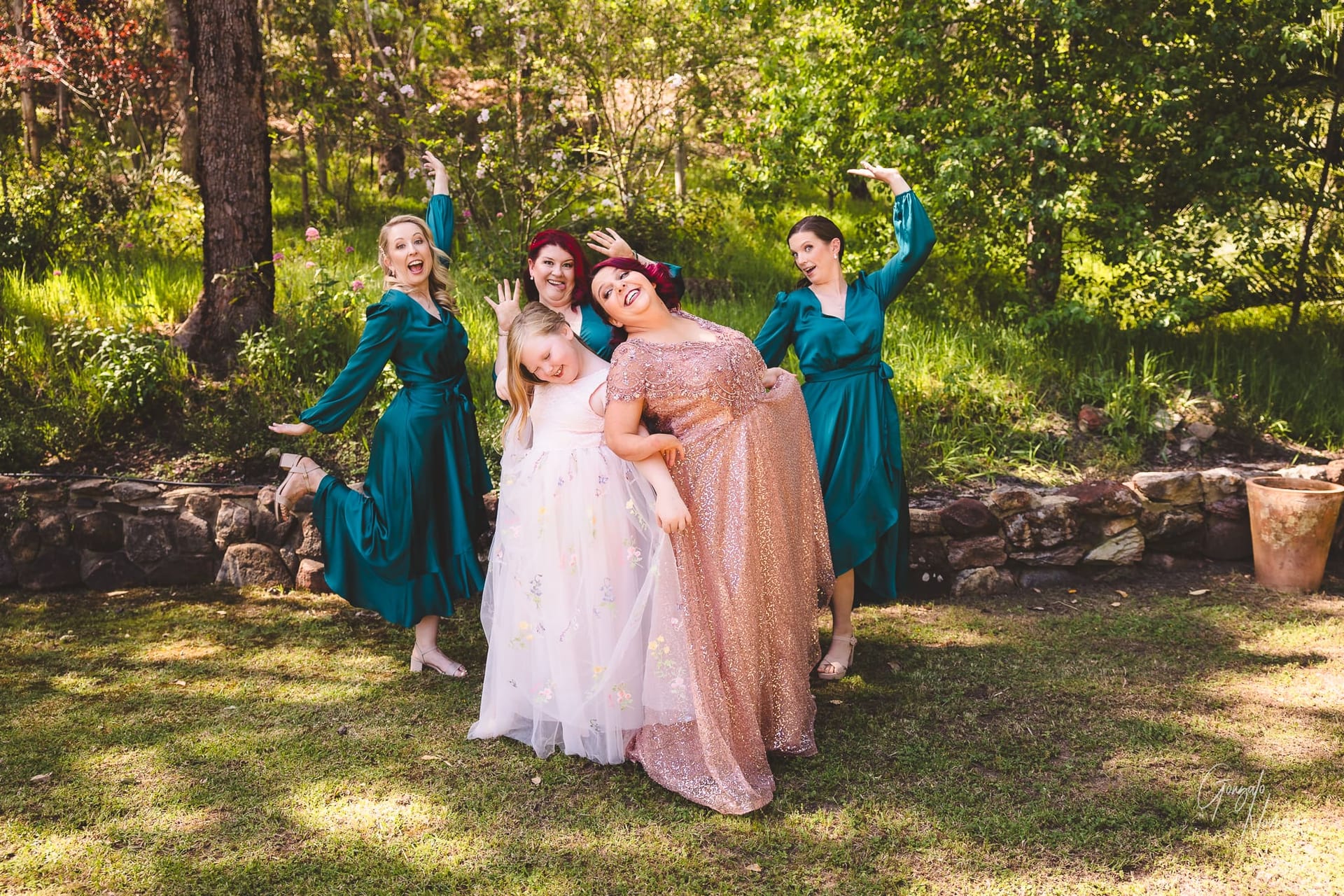 A group of bridesmaids smiling and posing for a photo in a picturesque woodland setting.