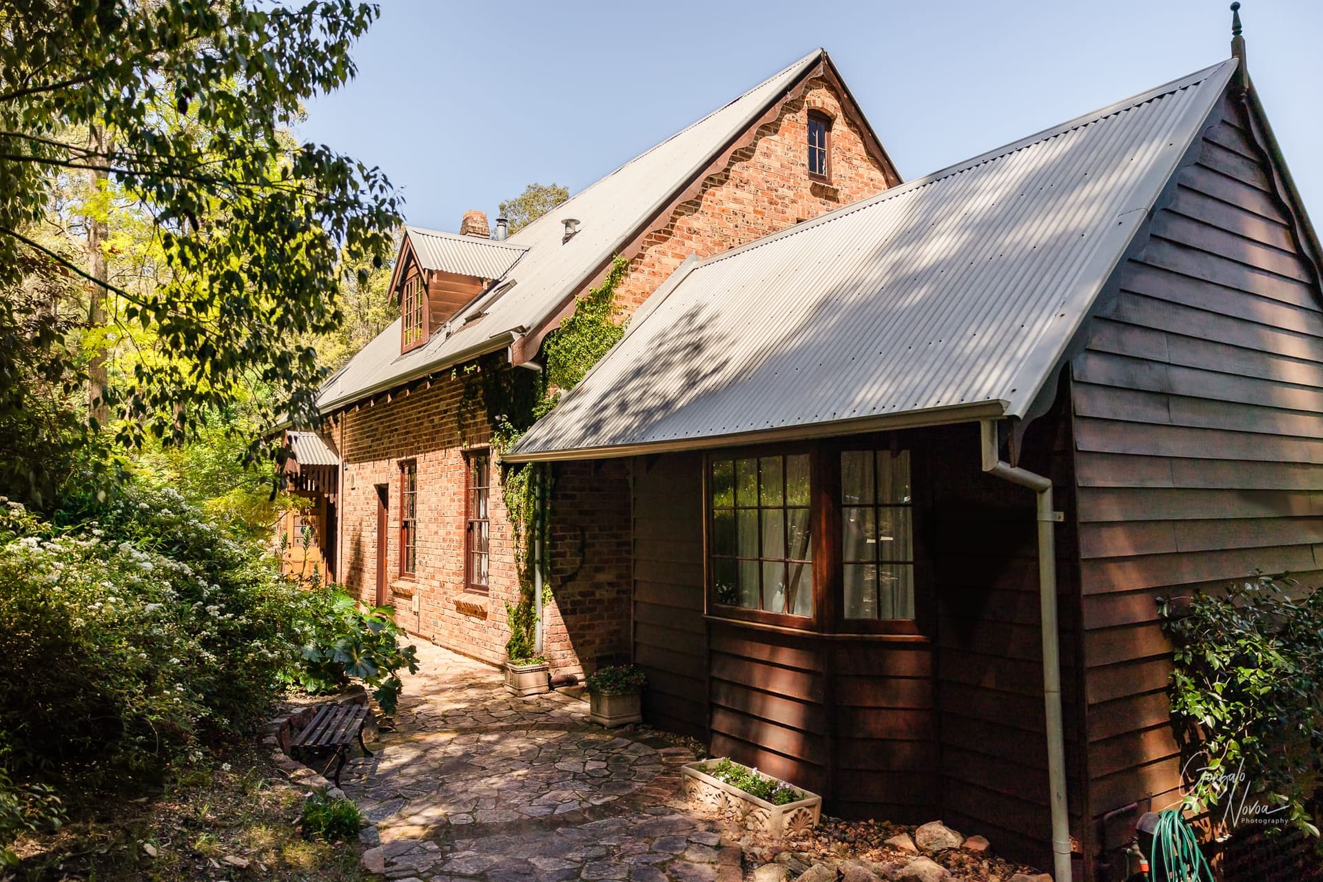 A house with a tin roof and stone path, surrounded by greenery.