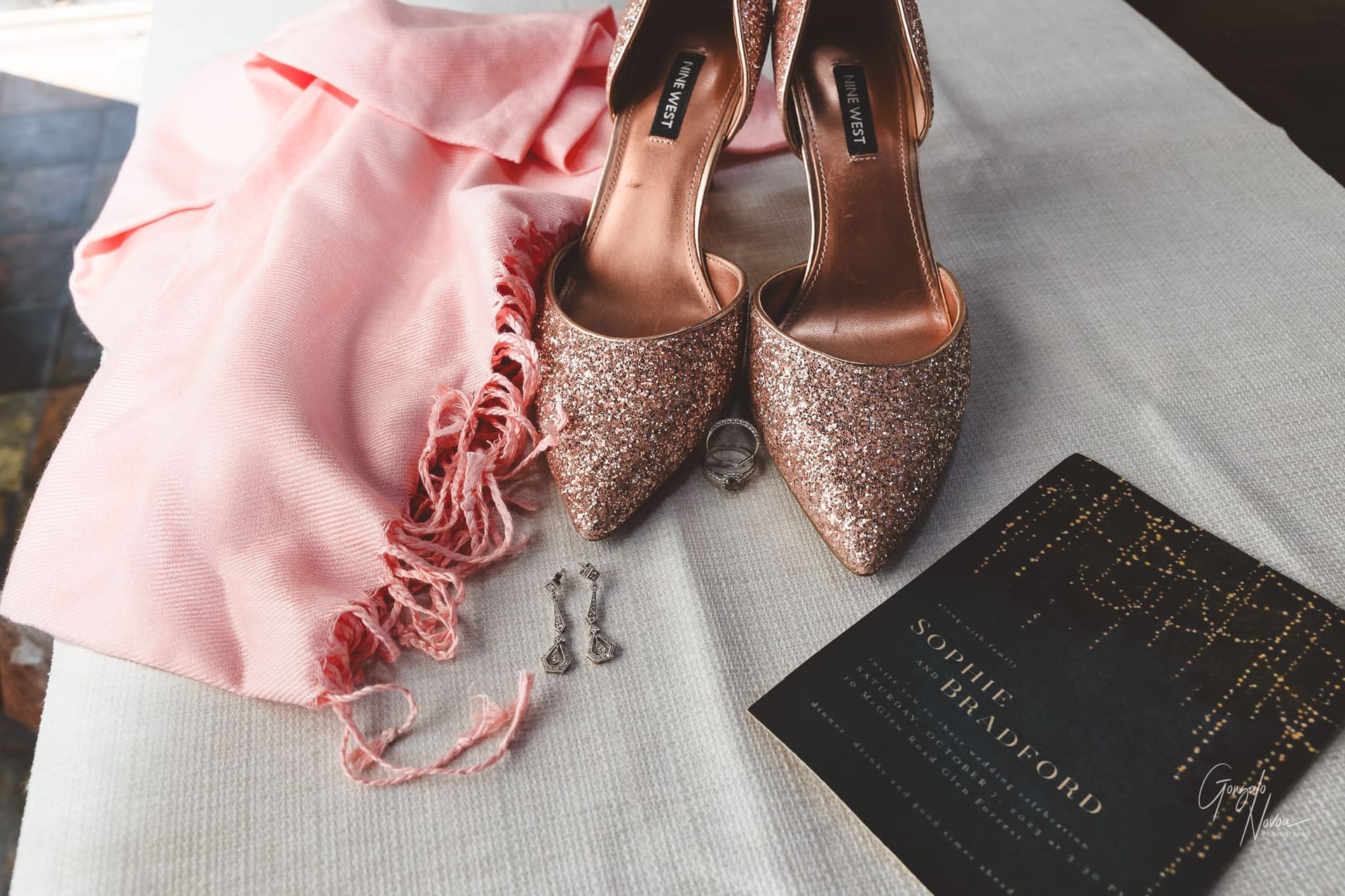 A photo of pink sparkly shoes, a pink scarf, and a the wedding invitation.