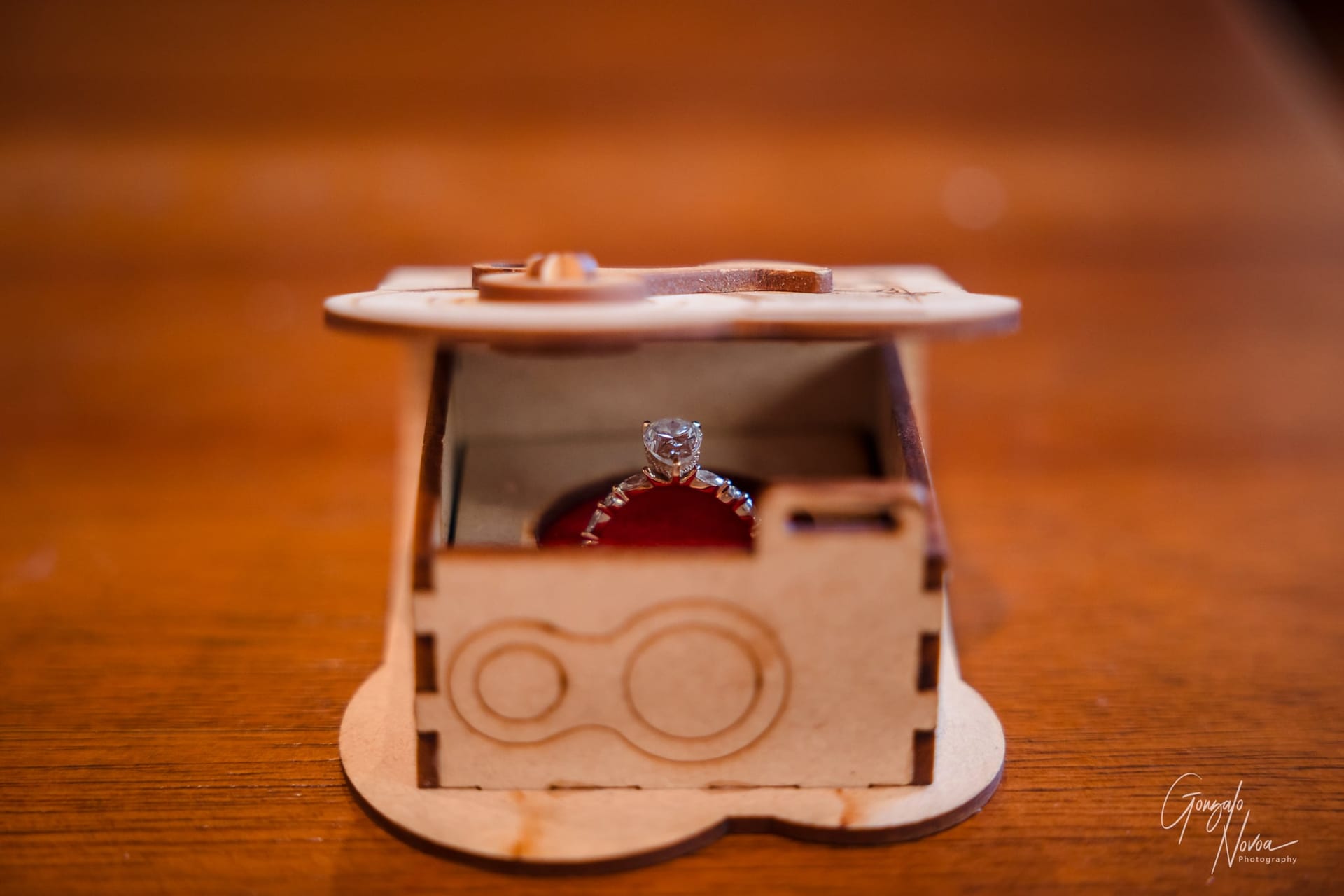 A diamond ring inside an open wooden box on a brown surface, conveying a romantic mood. Engraved design on box lid.